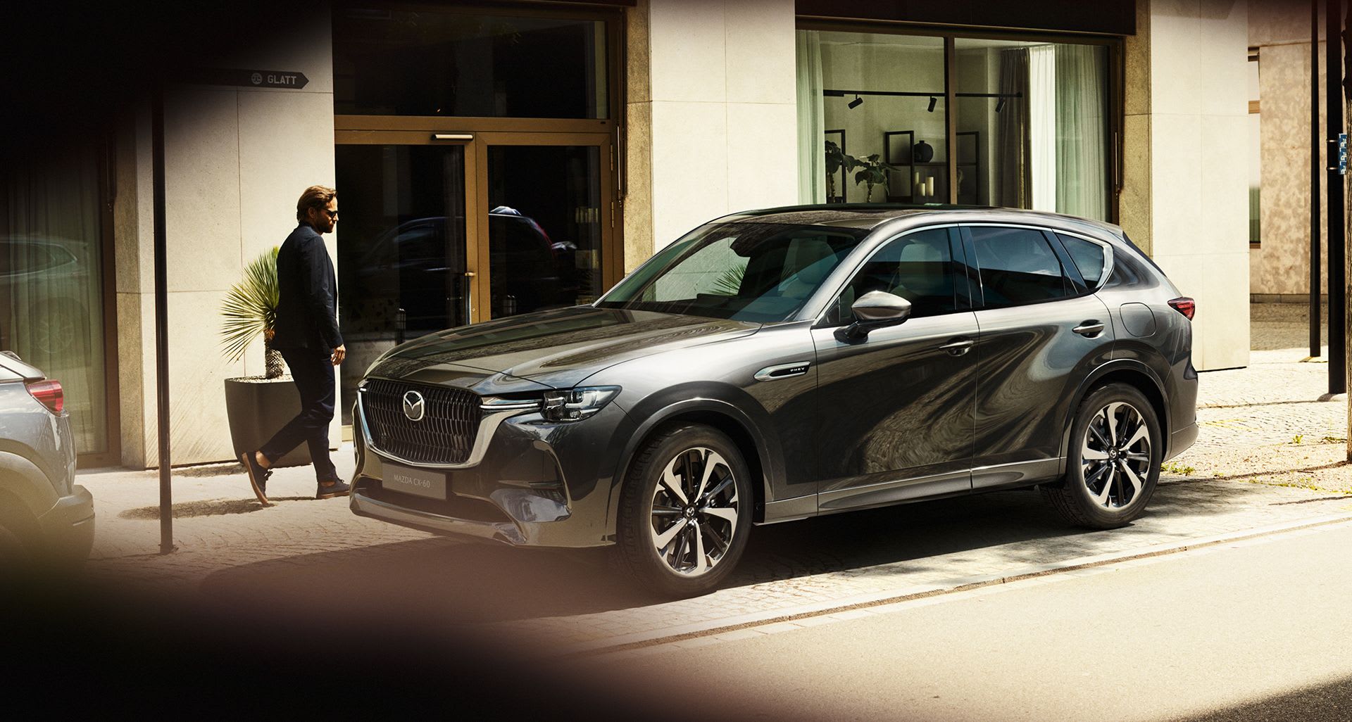 Grey Mazda CX-60 parked on a city street with a man walking by
