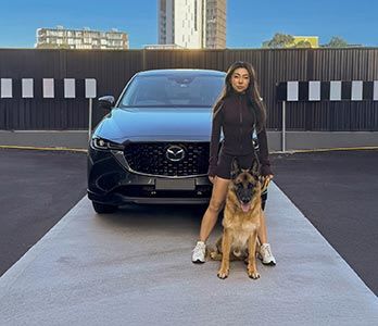 Woman with her German Shepherd standing in front of her Mazda 