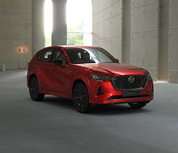 Front three quarter view of a Soul Red Mazda CX-60 SUV SP Hybrid parked in a gallery