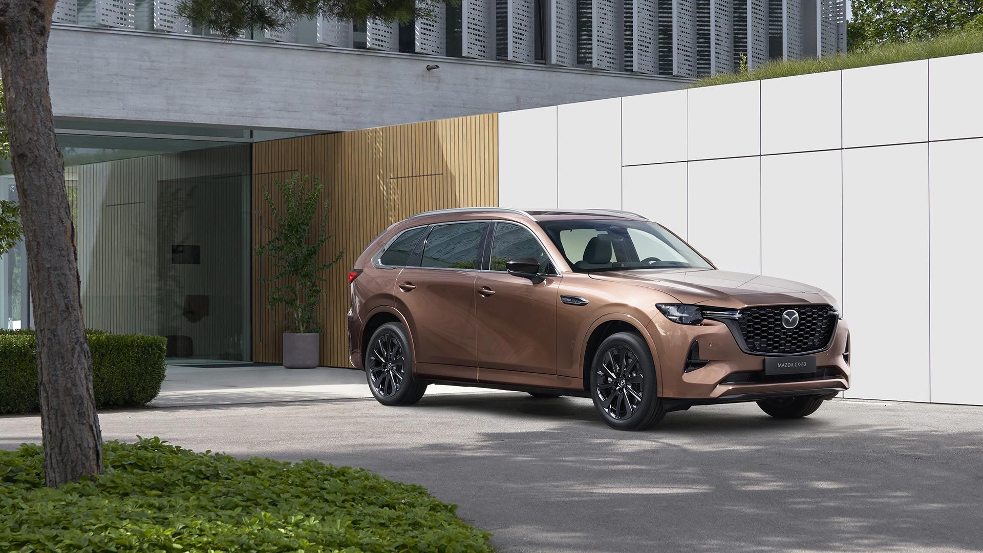 Front three quarter view of a Melting Copper Mazda CX-80 SUV parked in front of a designer house
