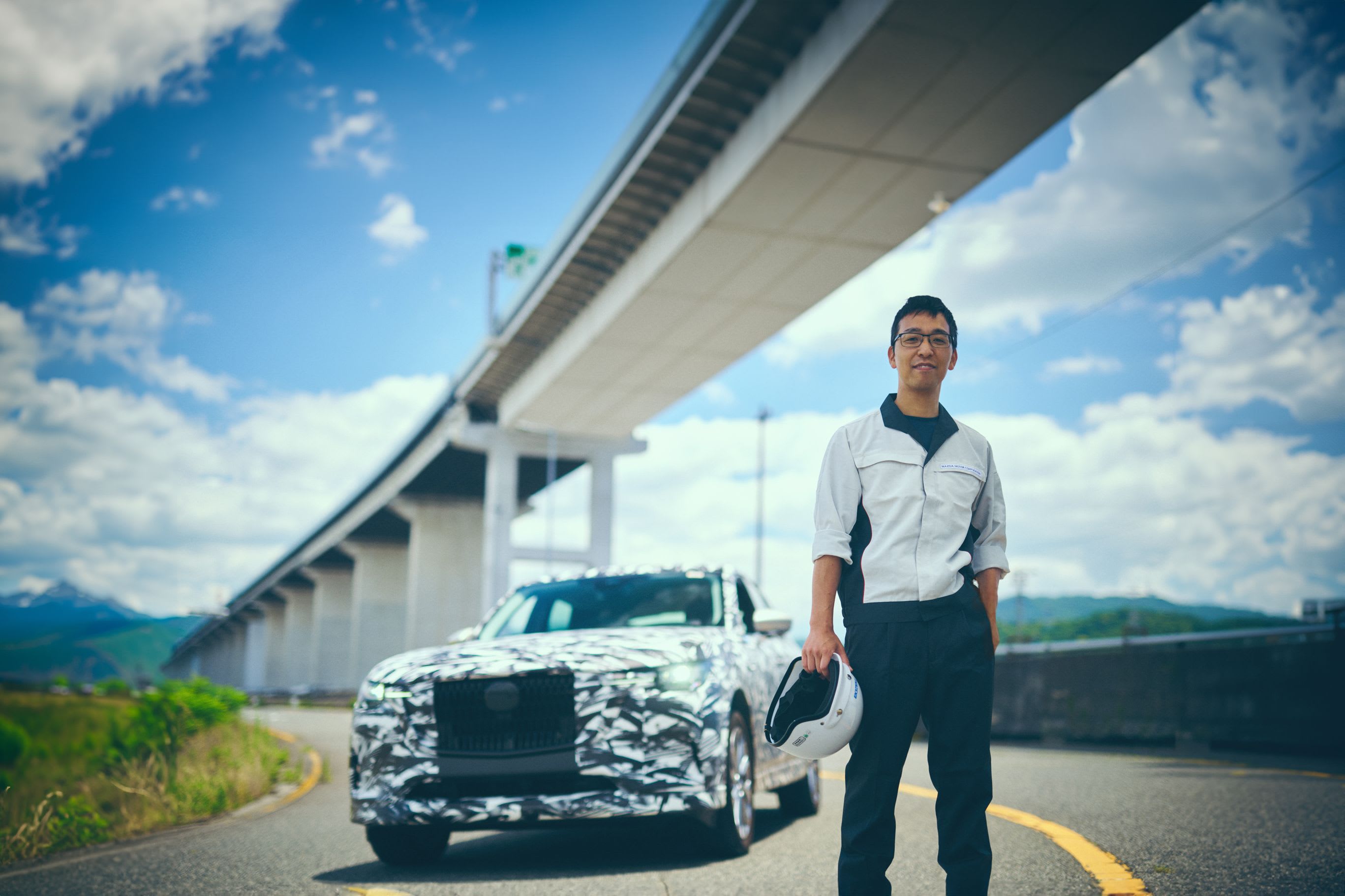 Mazda engineer standing next to a camouflaged Mazda on the Hiroshima headquarter's test track