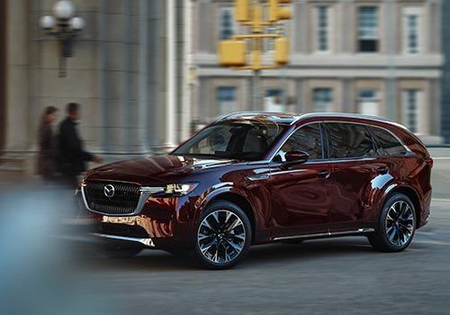 Front three quarter view of an Artisan Red Mazda CX-90 SUV parked in front of a heritage building