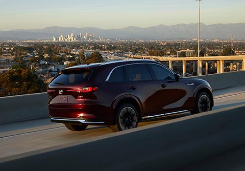 Rear three quarter view of an Artisan Red Mazda CX-90 SUV driving on a city overpass