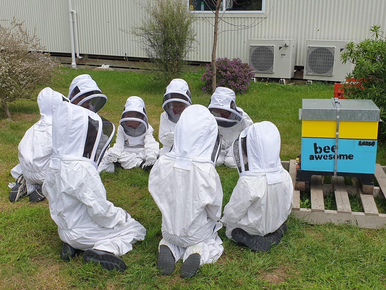 Beekeepers in protective clothing sitting in a circle next to a bee hive