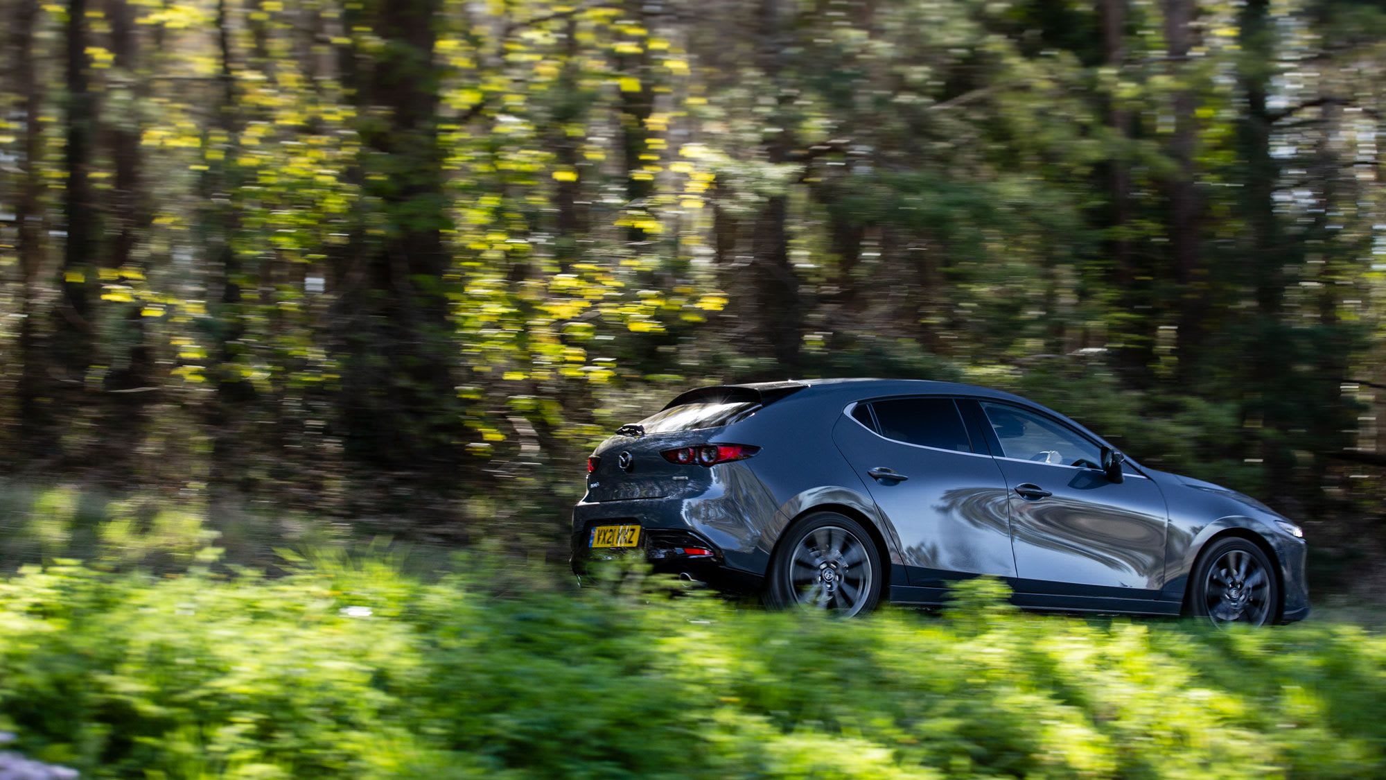 Grey Mazda3 hatchback driving through a forrest