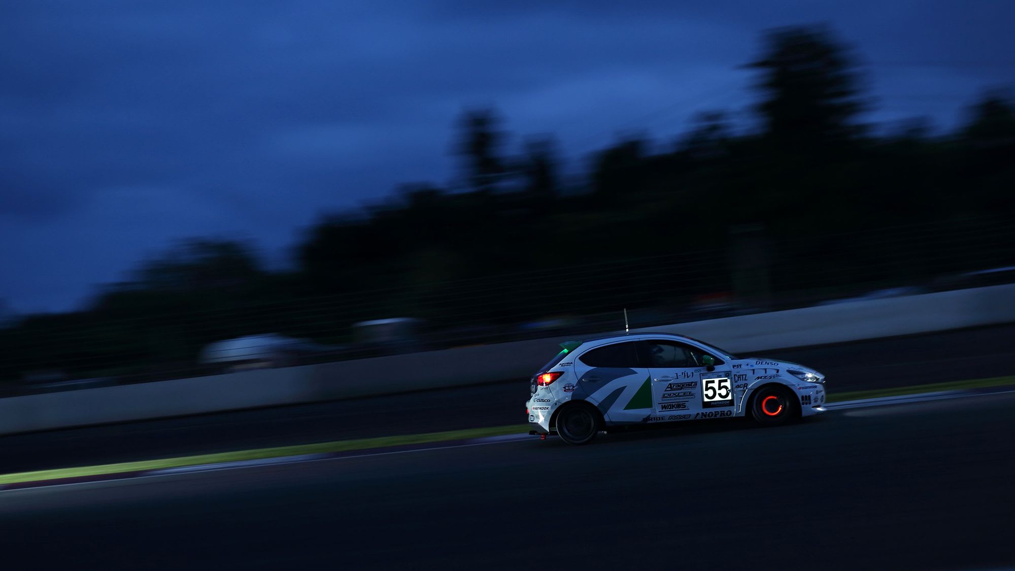 Side view of a Mazda2 Bio concept driving on a race track at dusk