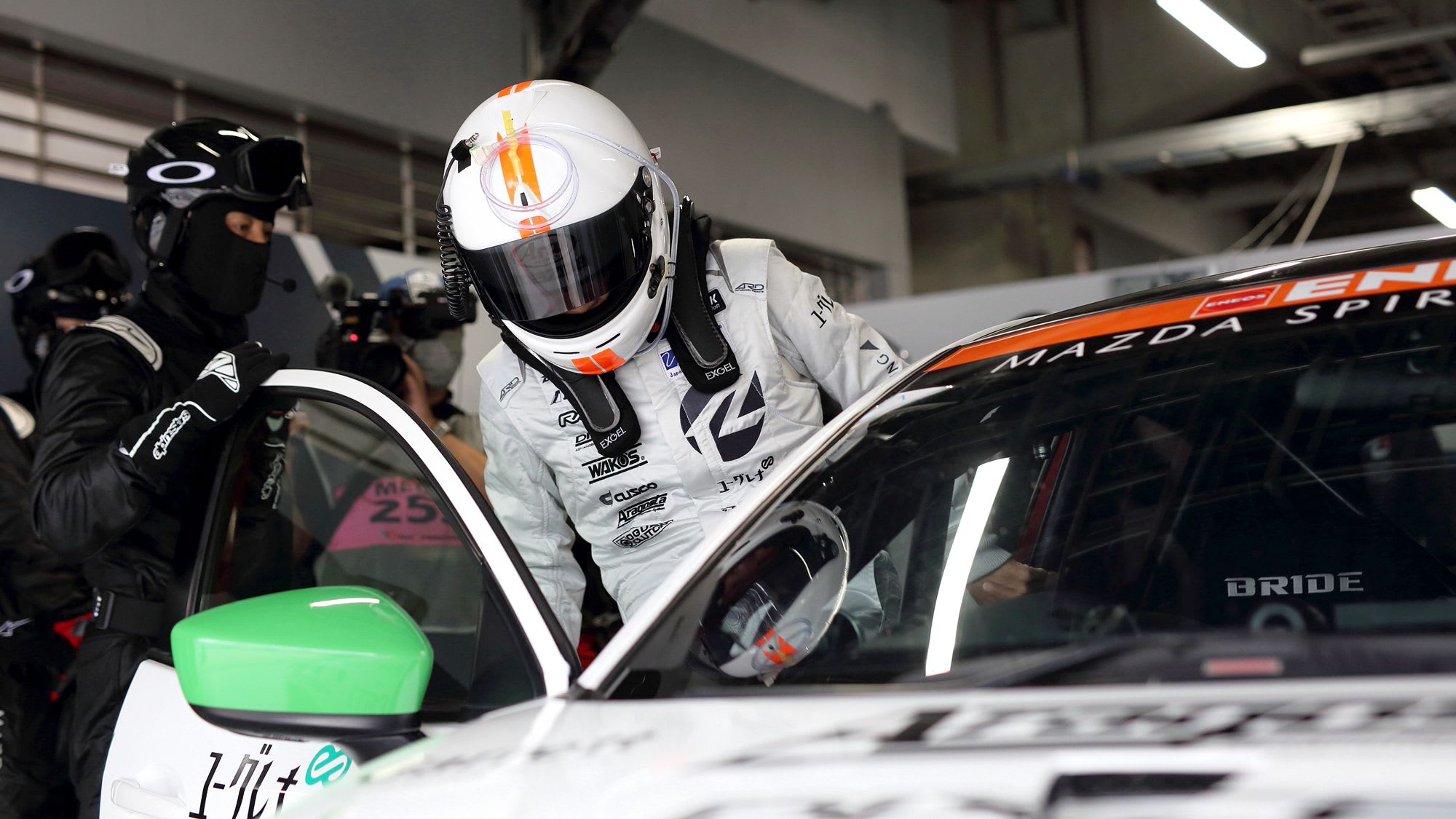 A race car driver wearing aa full face helmet getting into a Mazda2 Bio concept