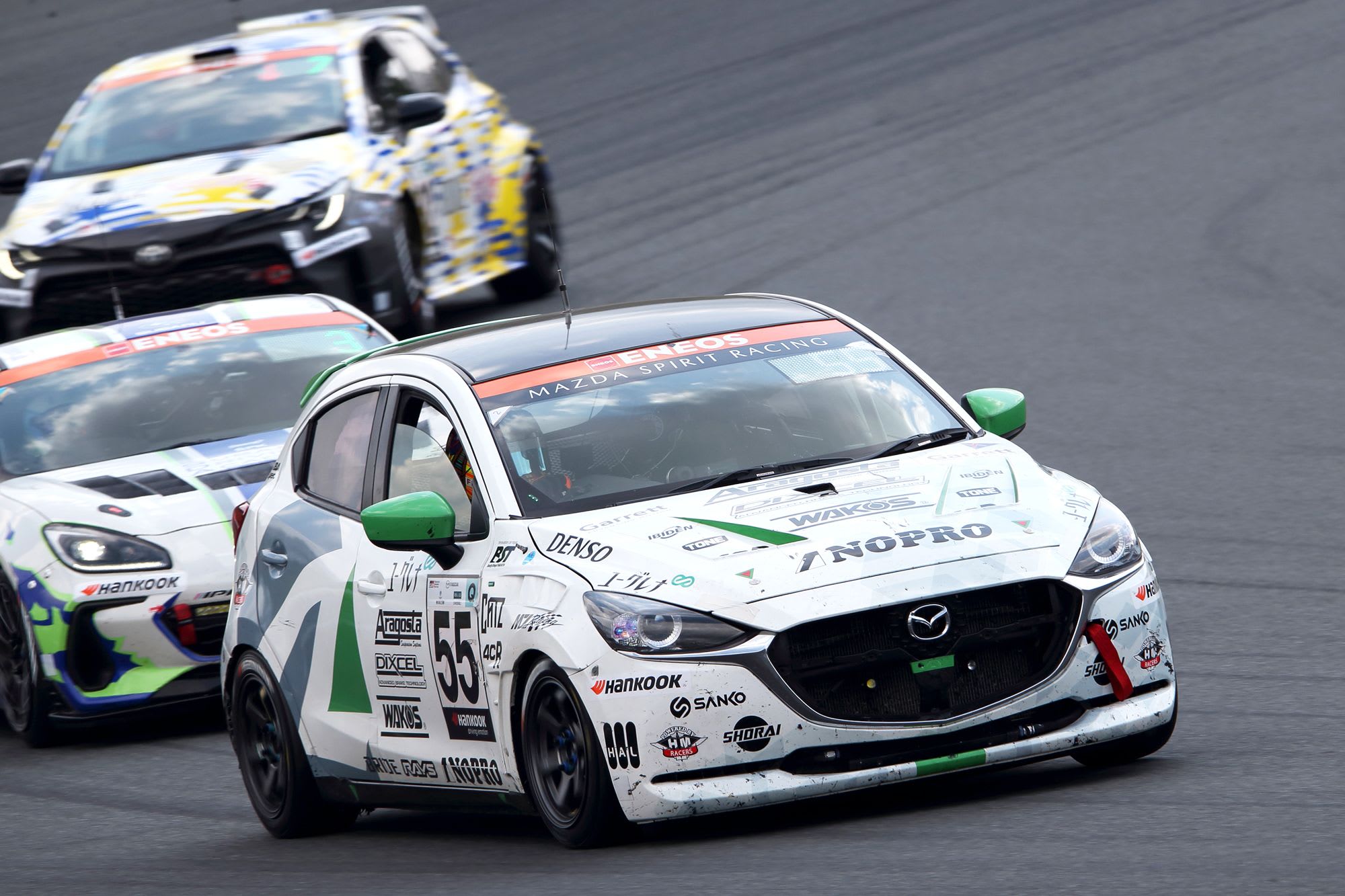 White Mazda2 Bio concept in a race going into a corner with two race cars following behind