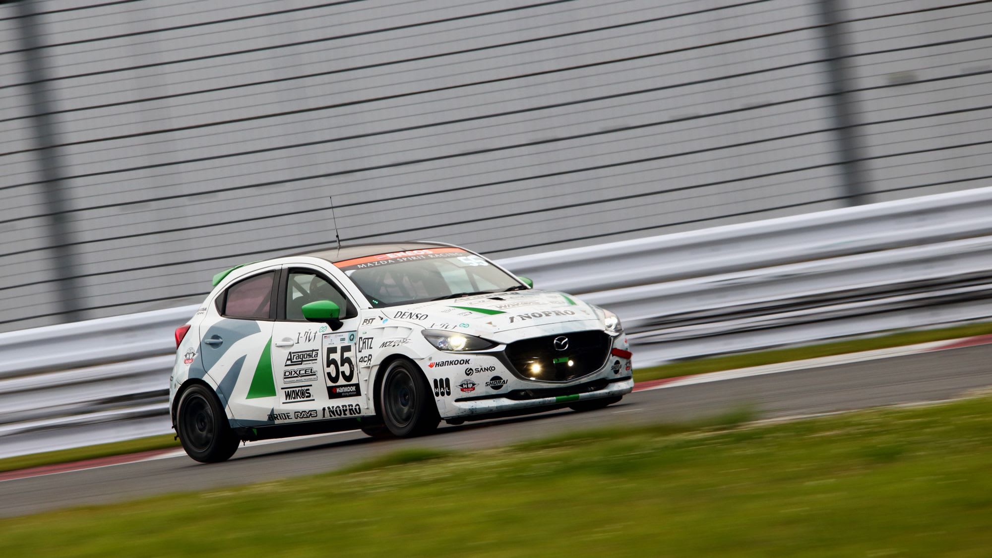 Front three quarter view of a white Mazda2 Bio race car driving on the track