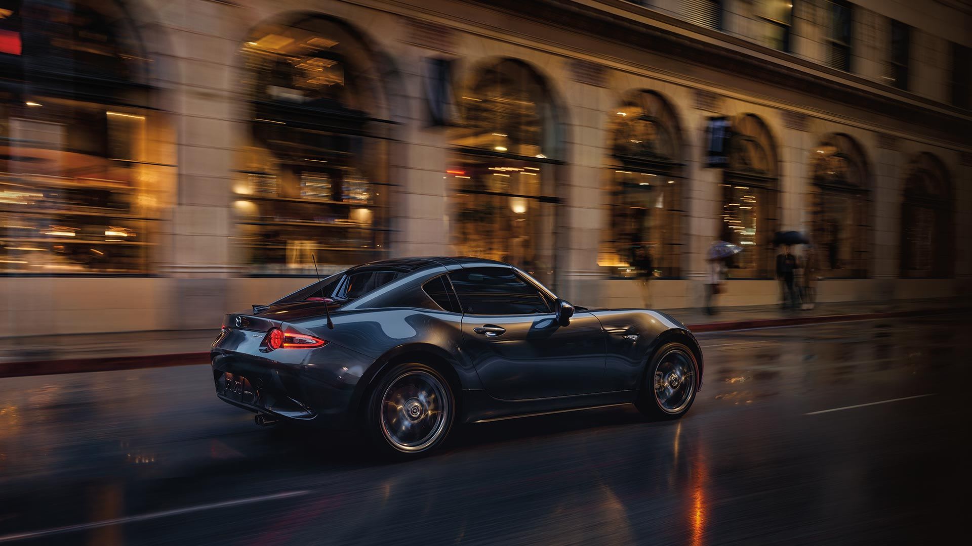 Rear three quarter view of a Machine Grey Mazda MX-5 RF driving on a city street