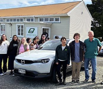 Youth driving trainees and training instructors standing next to a white Mazda MX-30 EV at Drive Outwest's training facility