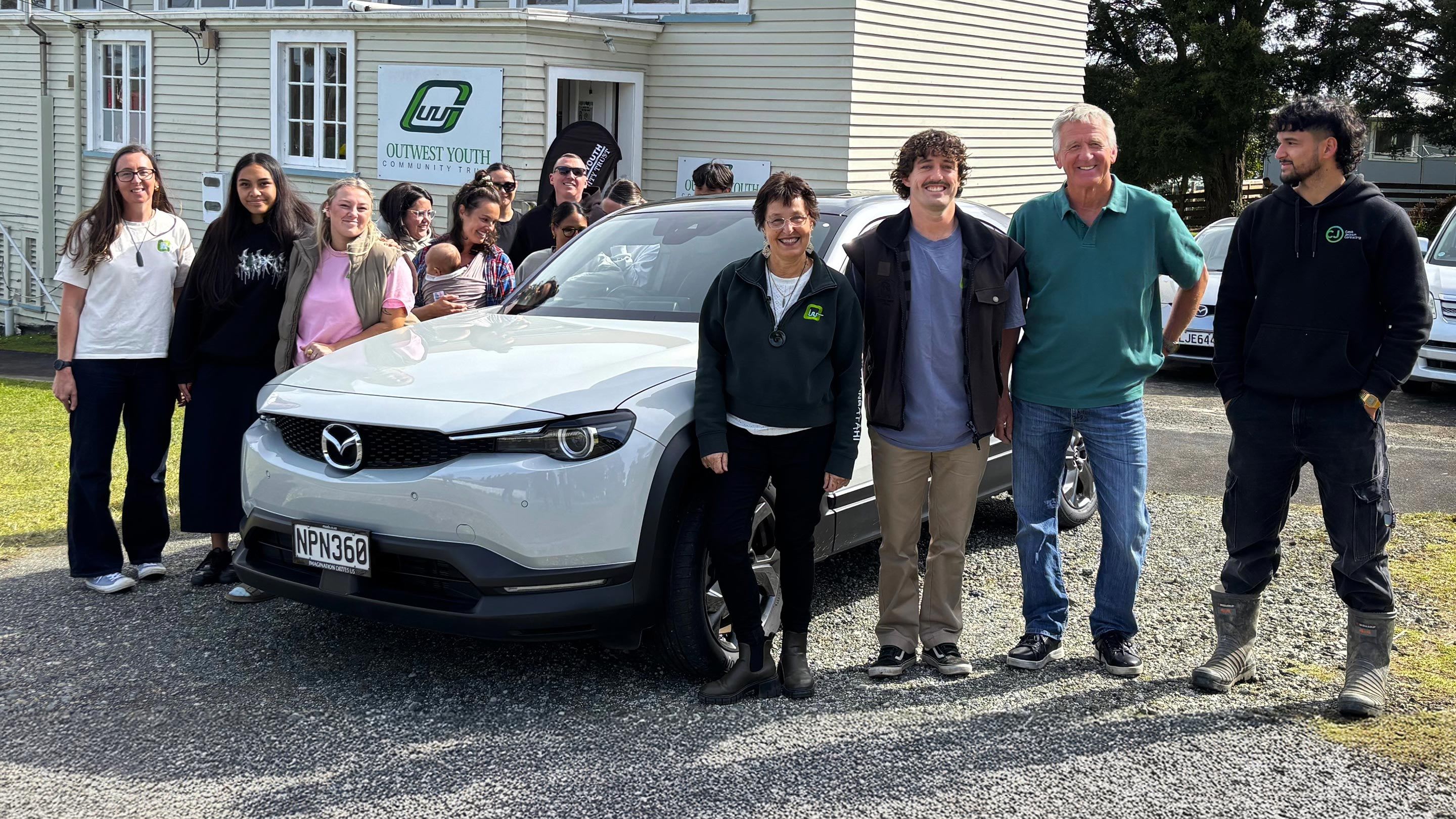 Youth driving trainees and training instructors standing next to a white Mazda MX-30 EV at Drive Outwest's training facility
