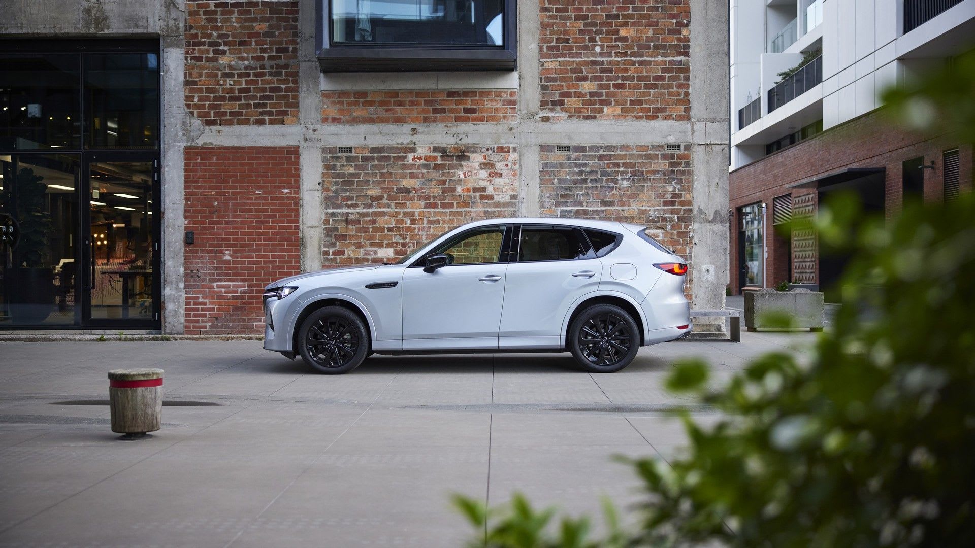 Side view of a Rhodium White Mazda CX-60 SUV parked in front of a brick building