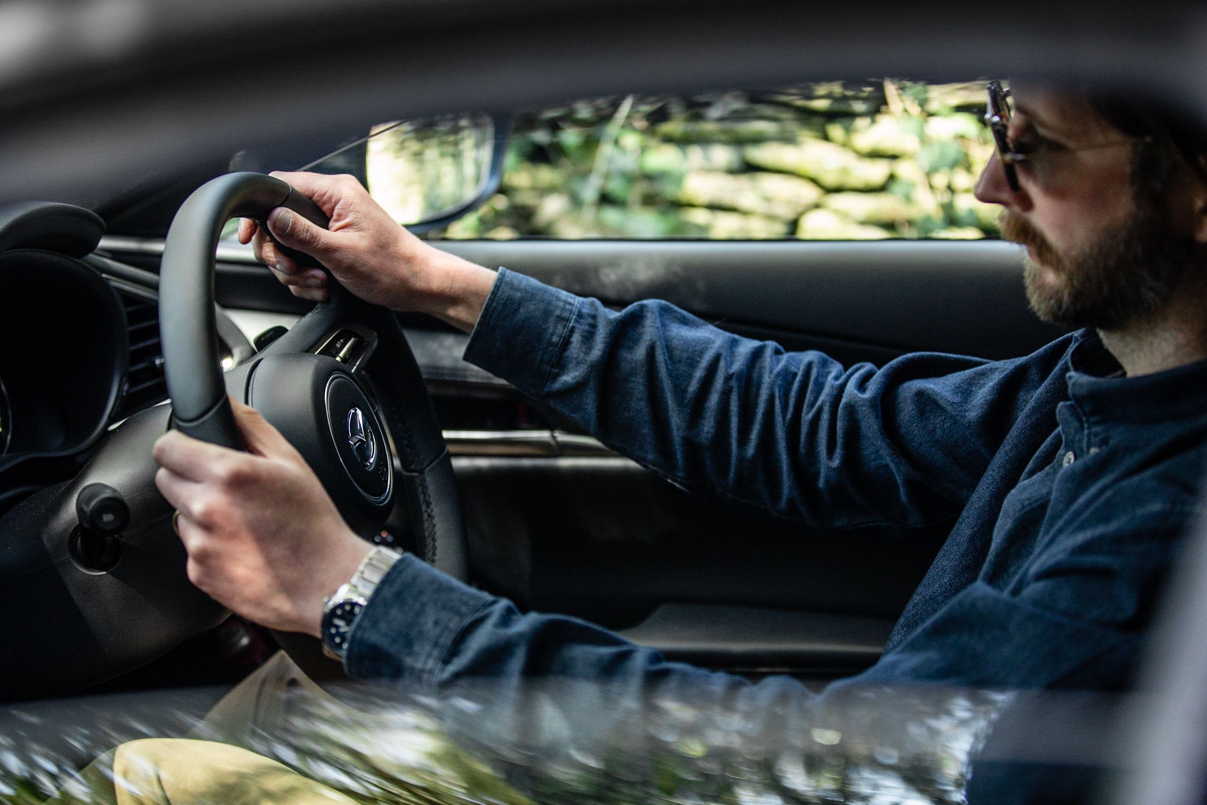Side view of a man in a blue shirt driving his Mazda car