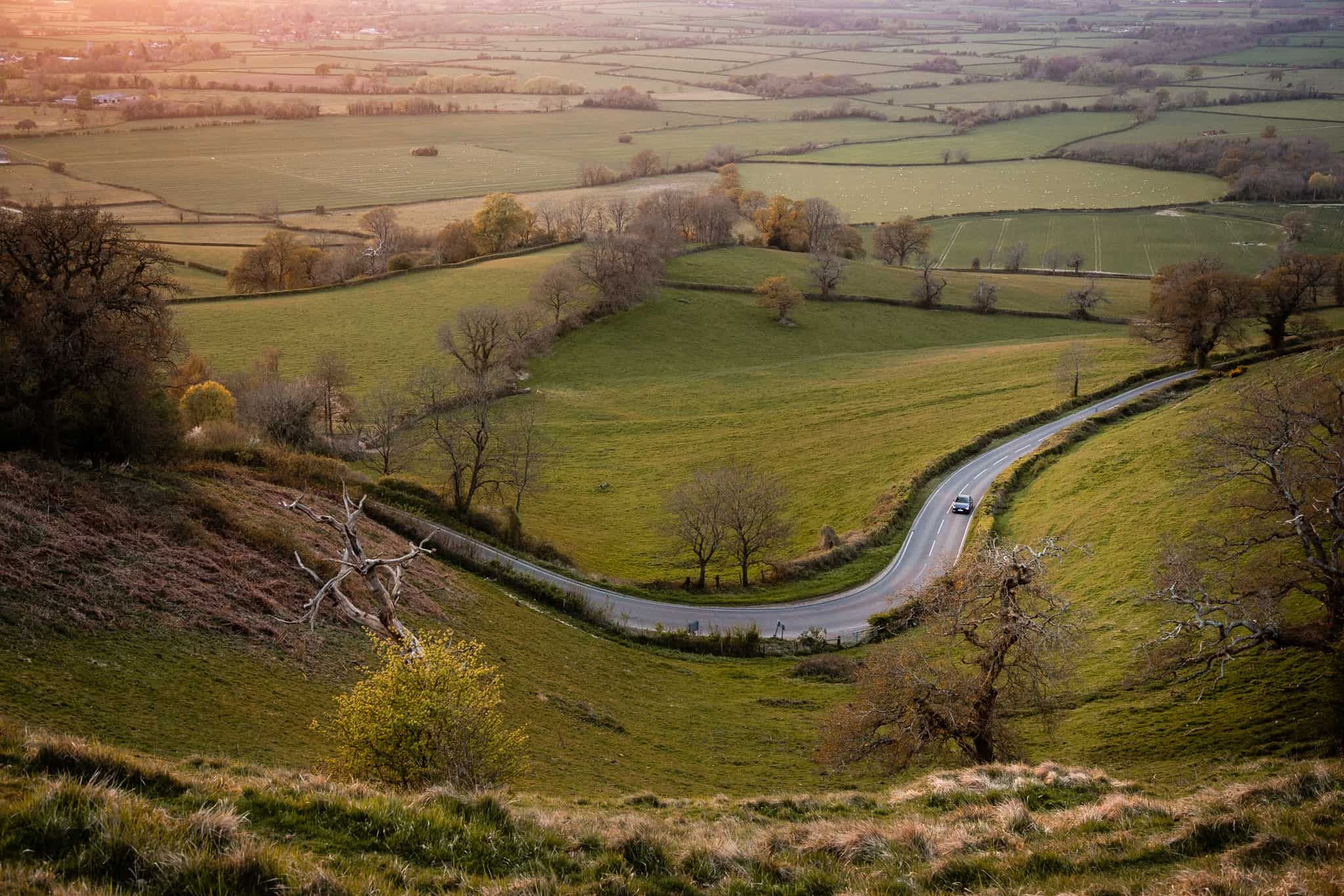 Far away view from up high looking down at a road winding through green hills with a grey Mazda3 driving
