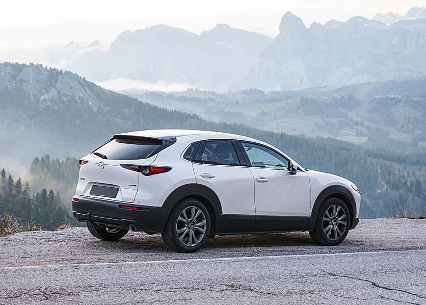 Rear three quarter view of a Snowflake White Mazda CX-30 SUV parked at a mountain lookout