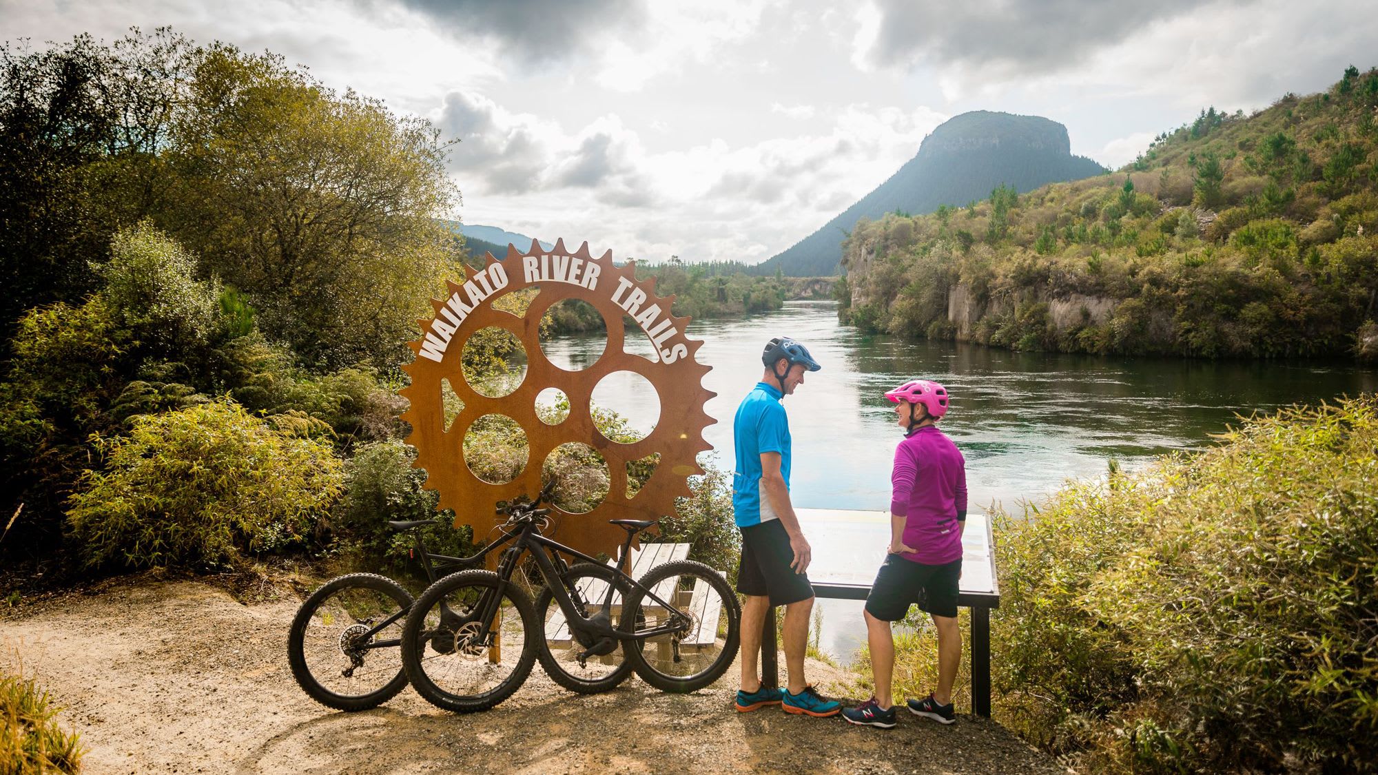 Two bikers standing next to their bikes next to the Waikato River Trails sign