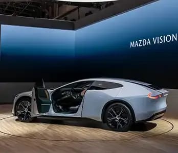 Rear three quarter view of a white Mazda Vision X-Coupe concept car with the front 'suicide door' open on a stand at the Japan Mobility  Show 2025