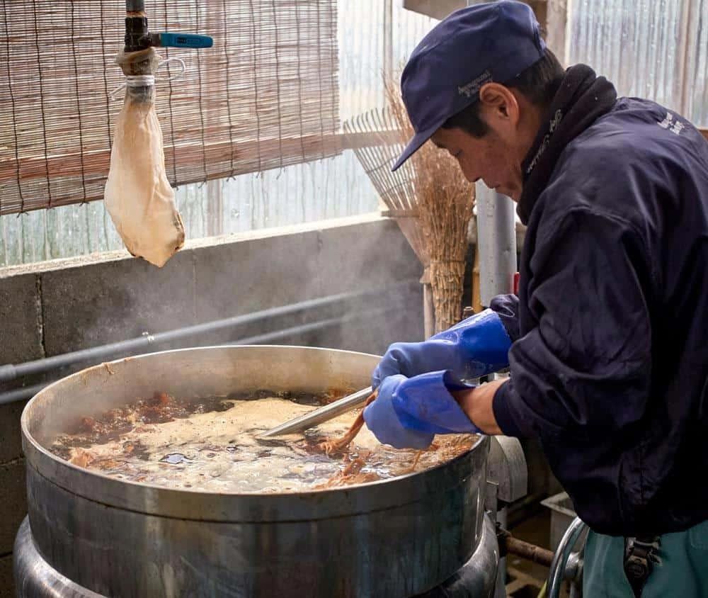 Man mixing bark in a large pot in the process of making traditional Japanese paper