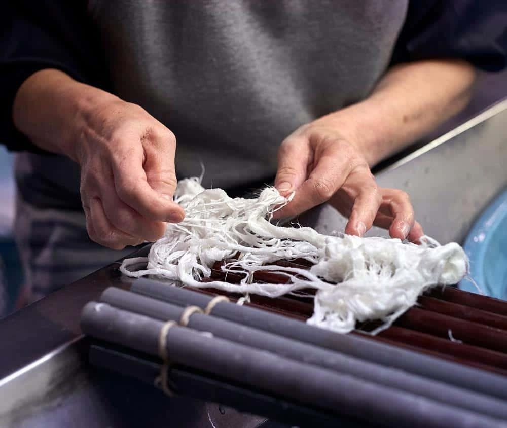 Close up of hands putting out fibres to dry in the process of making traditional Japanese paper