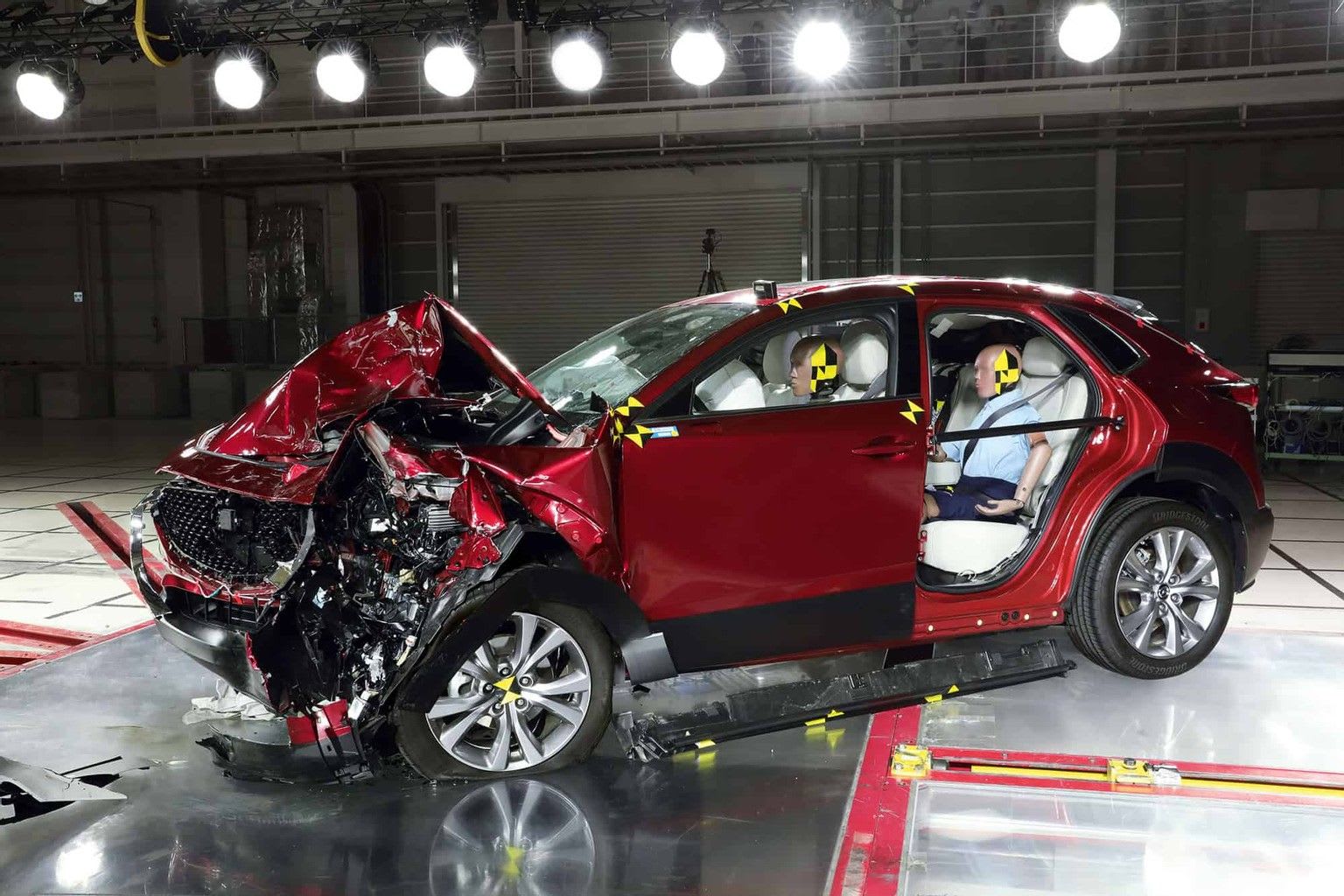 Red Mazda car in the crash test centre having just performed a crash test, showing a crumpled bonnet