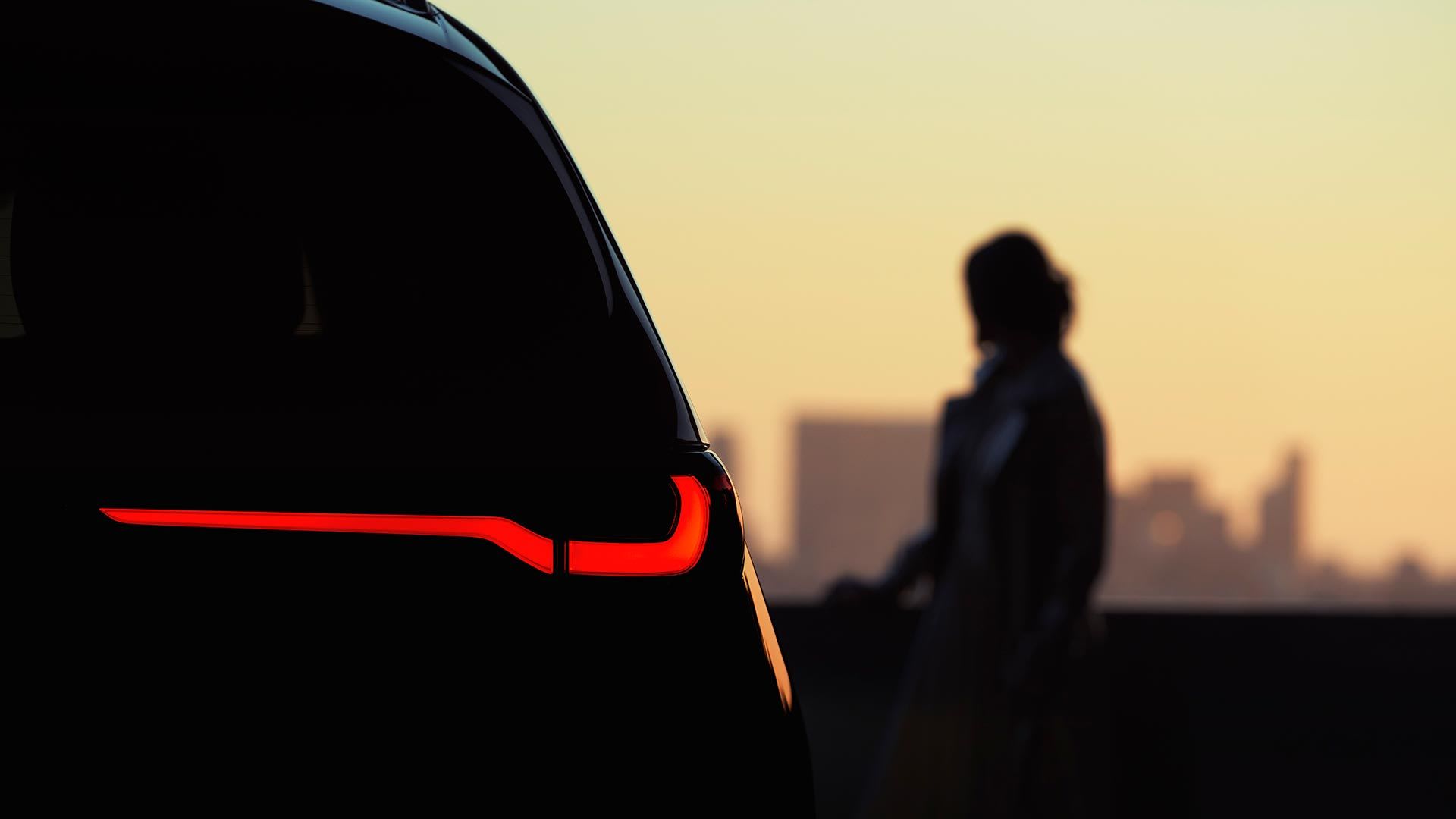 Silhouette of a woman standing next to the Mazda CX-90 SUV with its brake lights showing