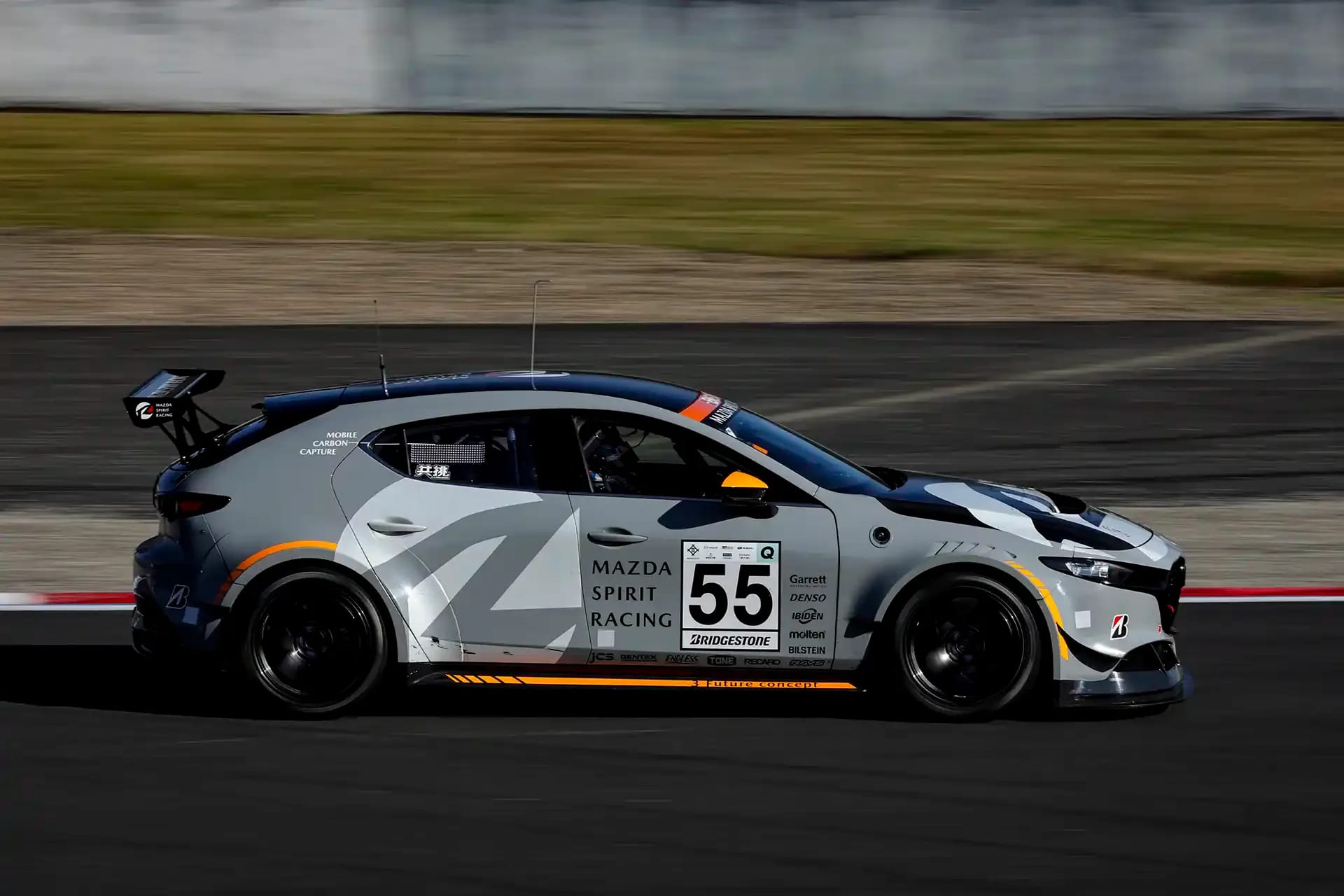 Side view of a grey Mazda3 race car on a race track in Japan