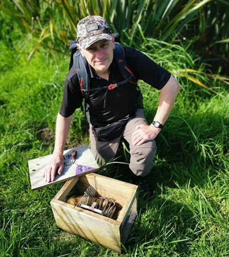 Man from the Environment Network Manawatu - Ian Rasmussen - kneeling on a grass field