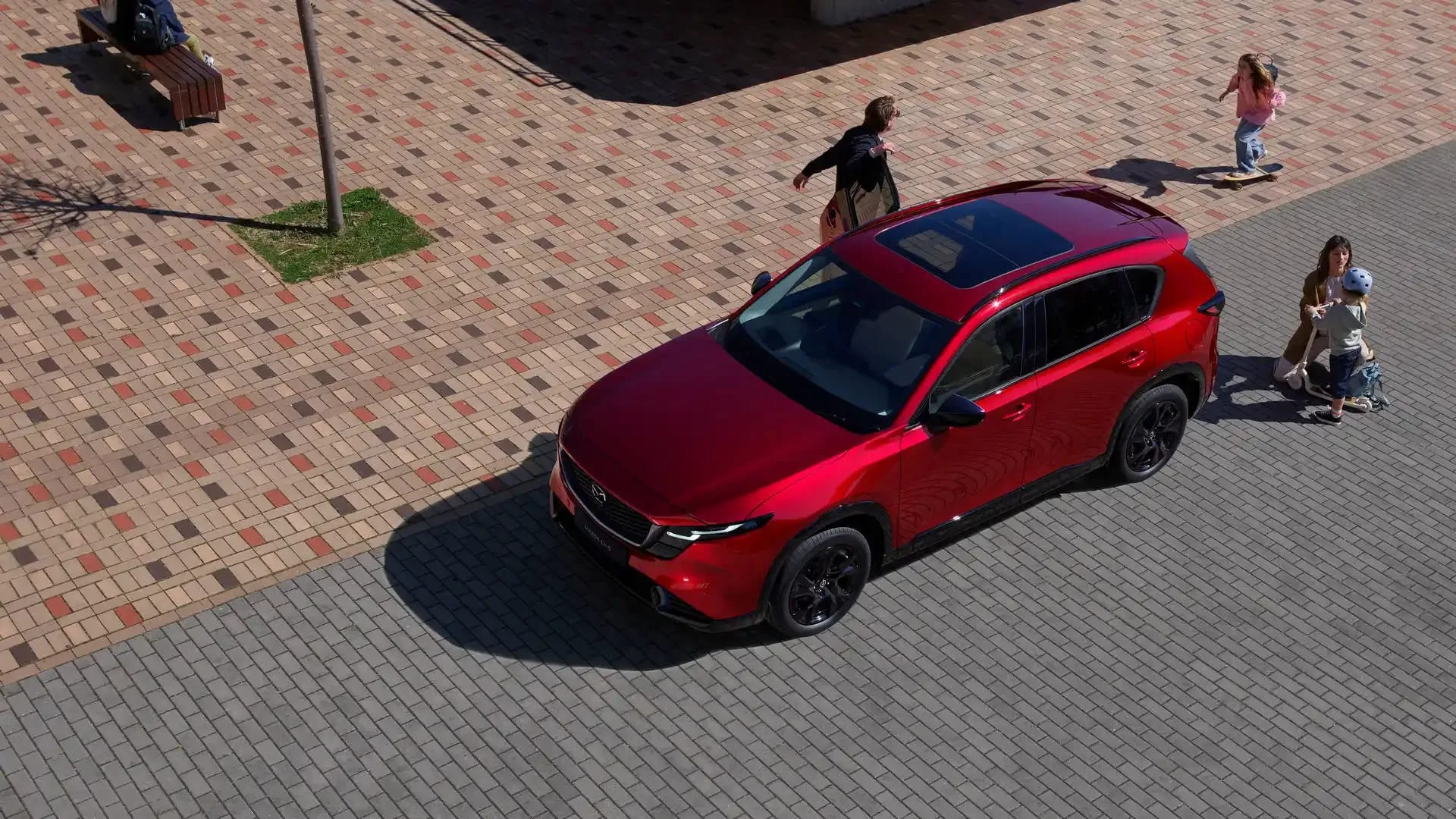 Front three quarter view from a height of a red Mazda CX-5 SUV with a man, woman and two young children around the car