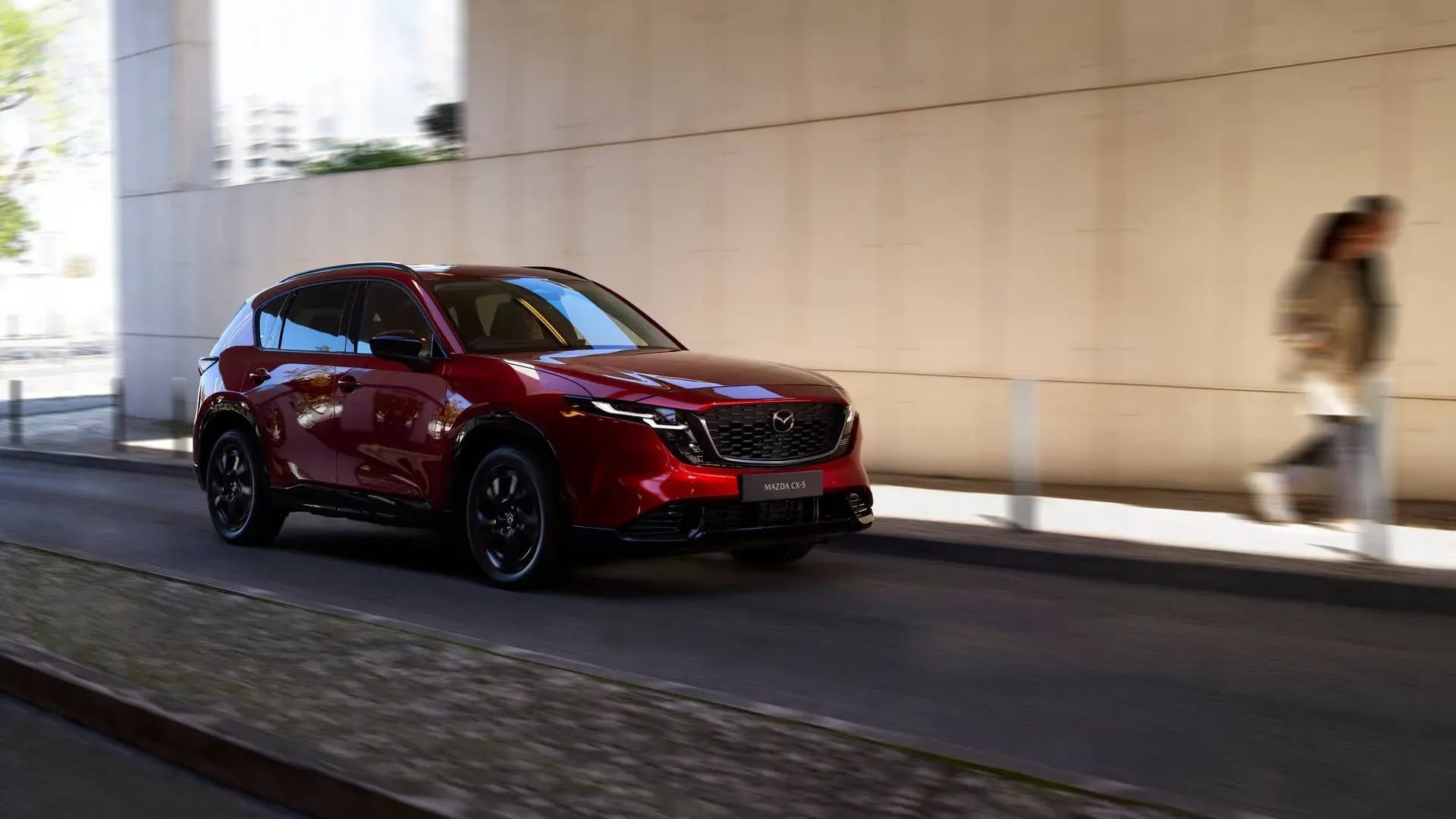 Front three quarter view of a red Mazda CX-5 driving down a city street