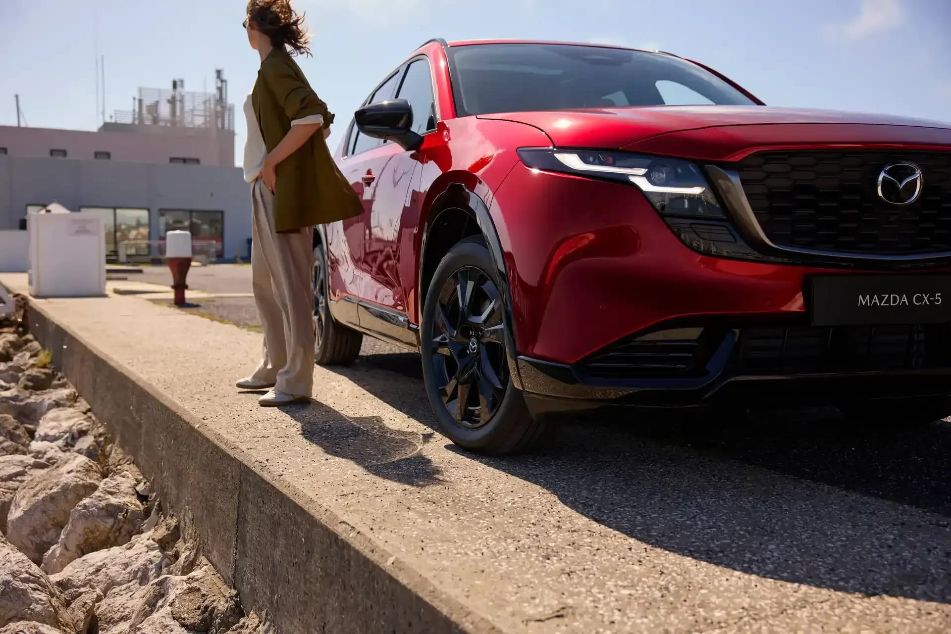 Front three quarter view of a Soul Red Mazda CX-5 SUV with a woman standing next to the car