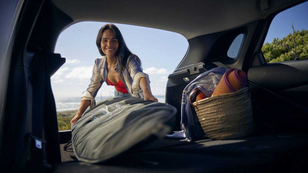 A woman loading a surfboard into the back of a Mazda CX-30
