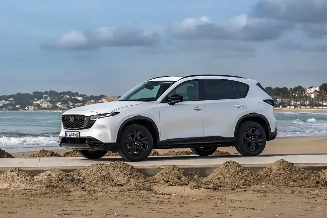 Front side view of a white all-new Mazda CX-5 SUV parked in front of a beach