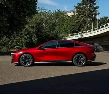 Side view of a Soul Red Mazda 6e electric car parked under a freeway offramp
