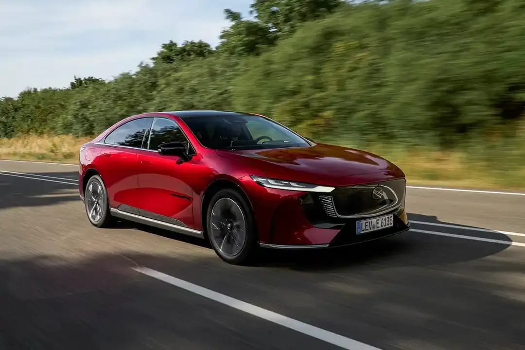 Front three quarter view of a Soul Red Mazda 6e electric car driving on an open road