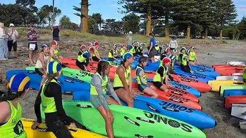 Members of the Waikanae Surf Life Saving Club line up on the beach with surf skis 