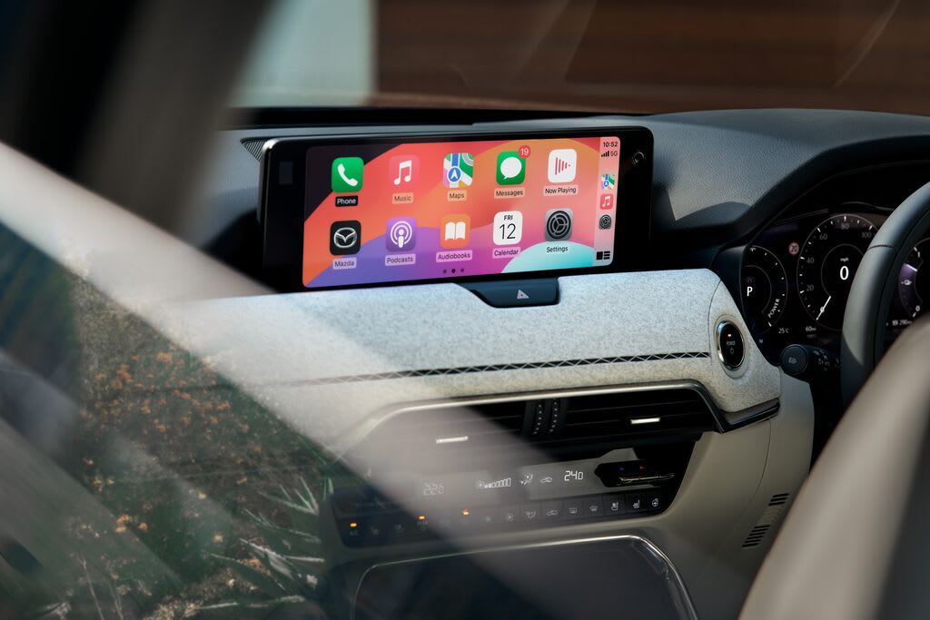 Close-up of the Mazda CX-80 7-seat hybrid SUV's touchscreen connected to a smartphone displaying the phone's apps