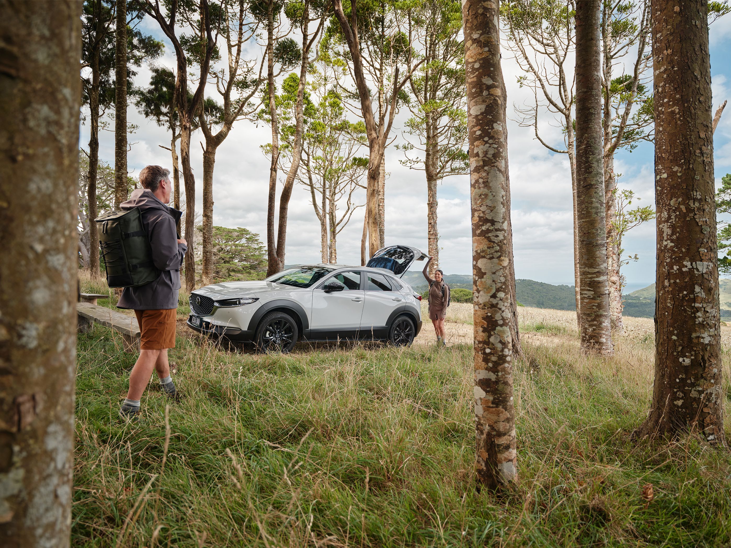 A couple gets ready to hit the road in their Ceramic Metallic Mazda CX-30 after finishing a hike in the country.