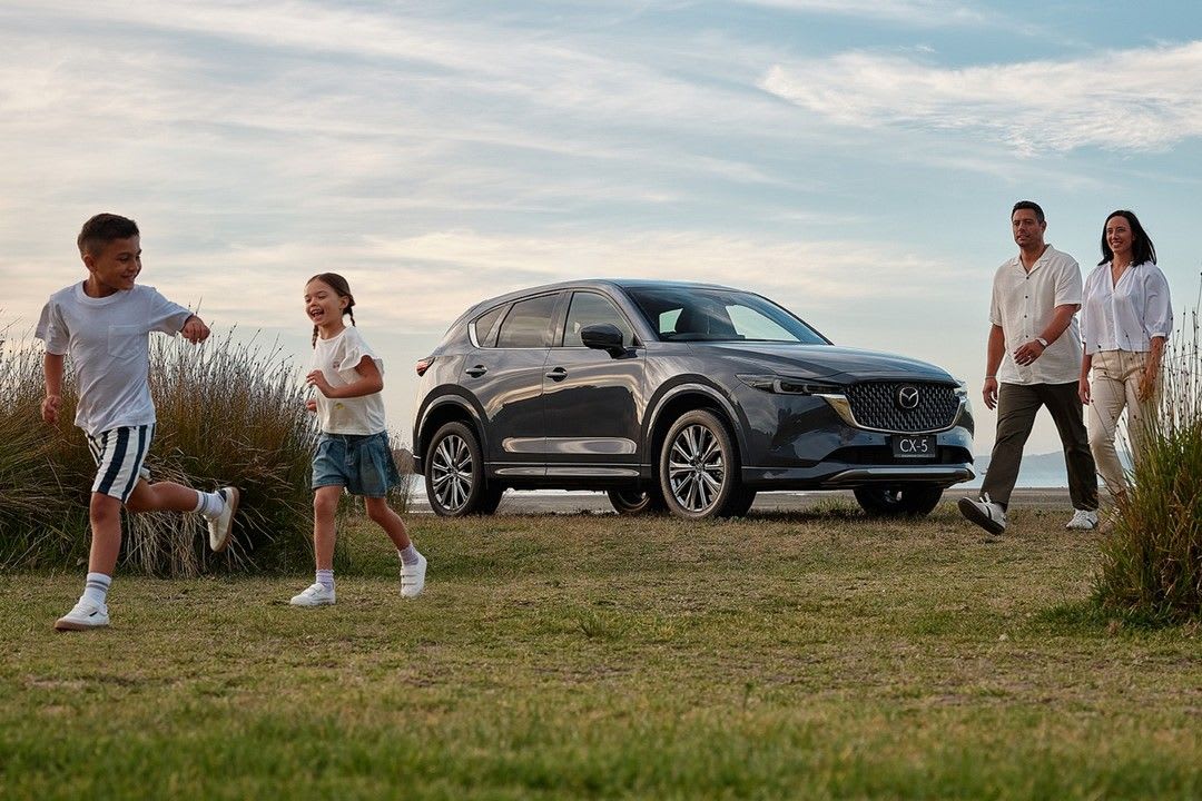 A family walking past their Machine Grey Metallic Mazda CX-5, parked near the water.