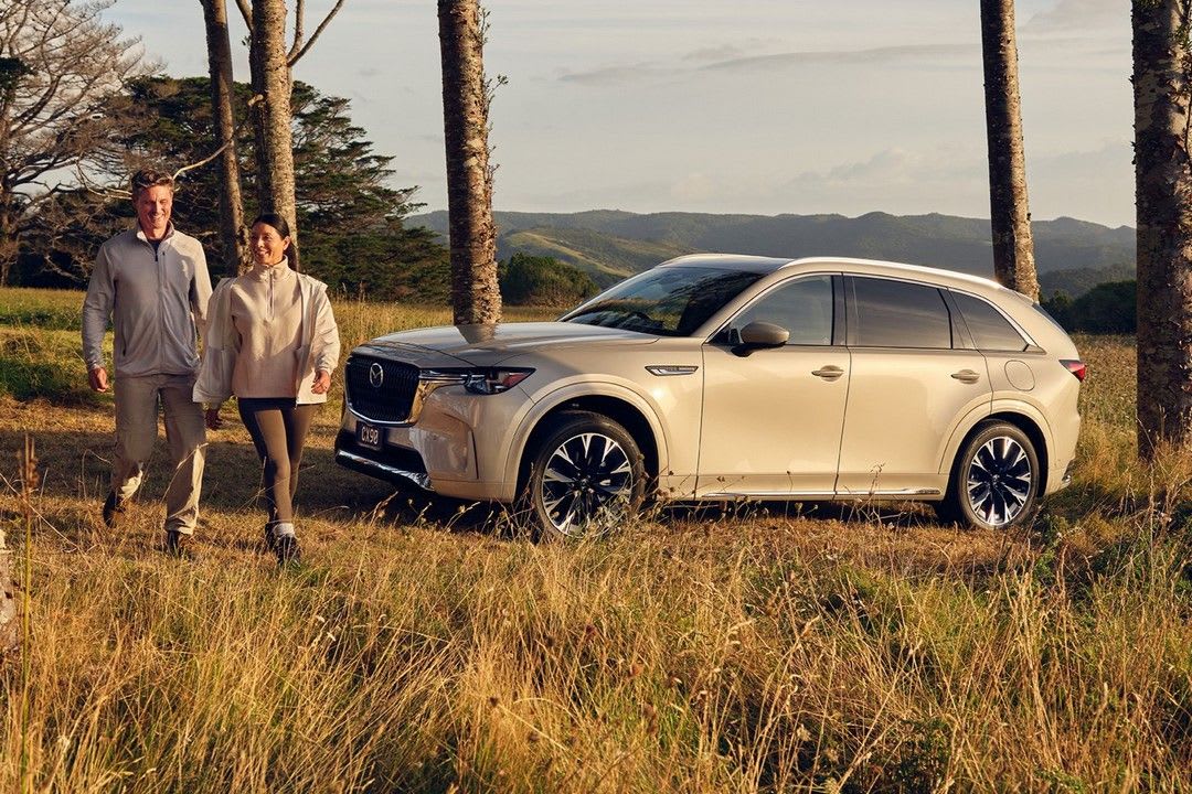 A couple walking past their Platinum Quartz Metallic Mazda CX-90 as they go for a stroll in the country