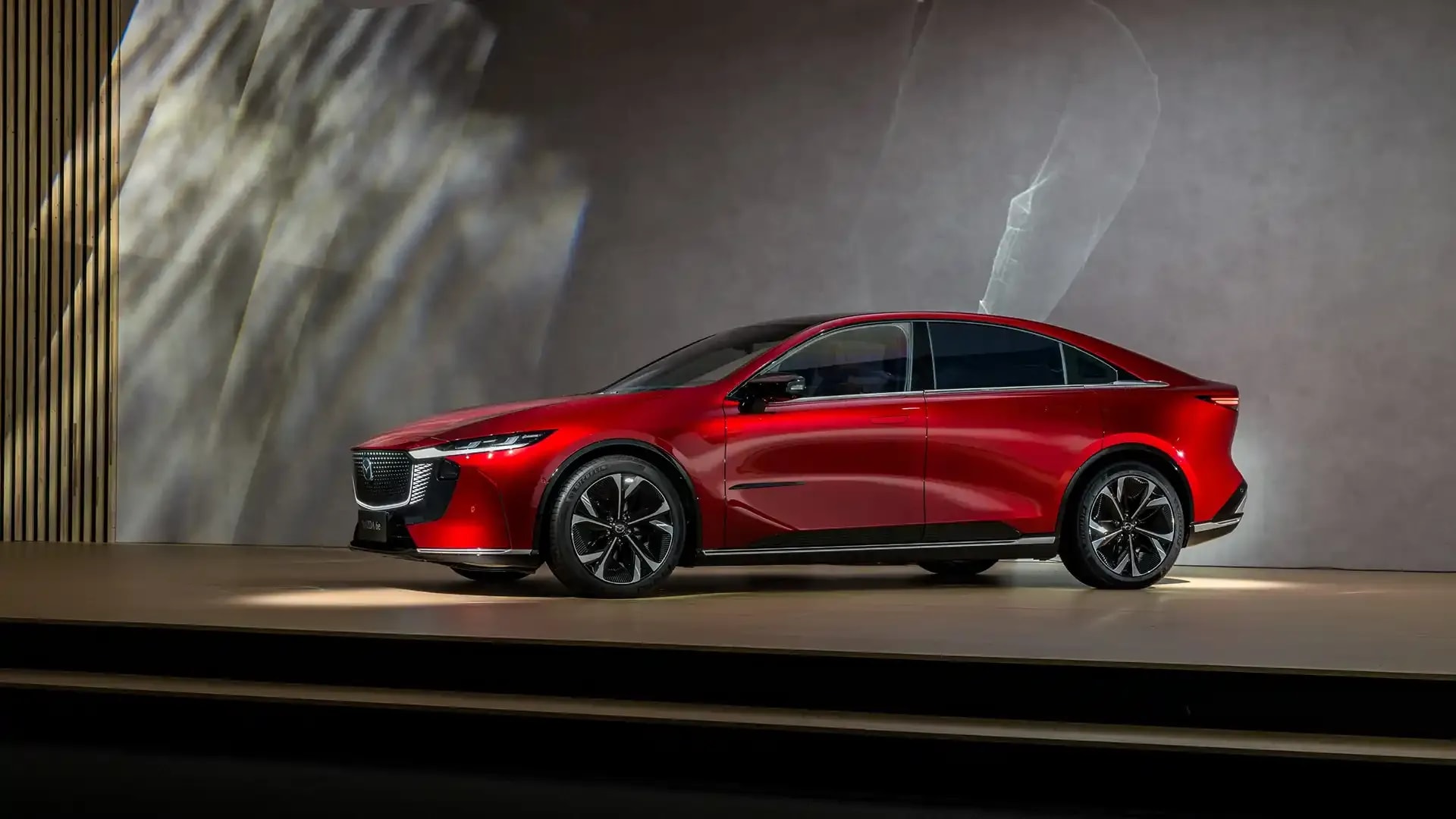 Side view of a Soul Red Mazda 6e electric vehicle on display in a gallery