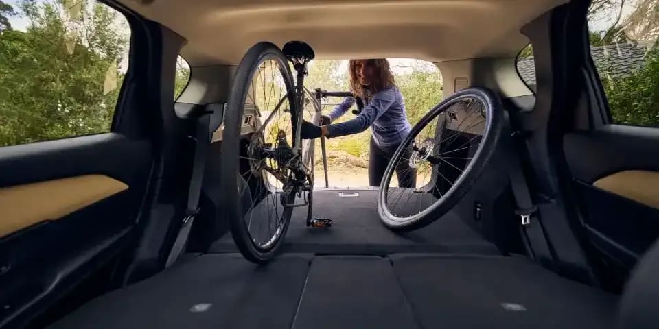 Looking back through the folded seats and the open tailgate of a Mazda CX-5 SUV with a woman loading a mountain bike into the back of the car