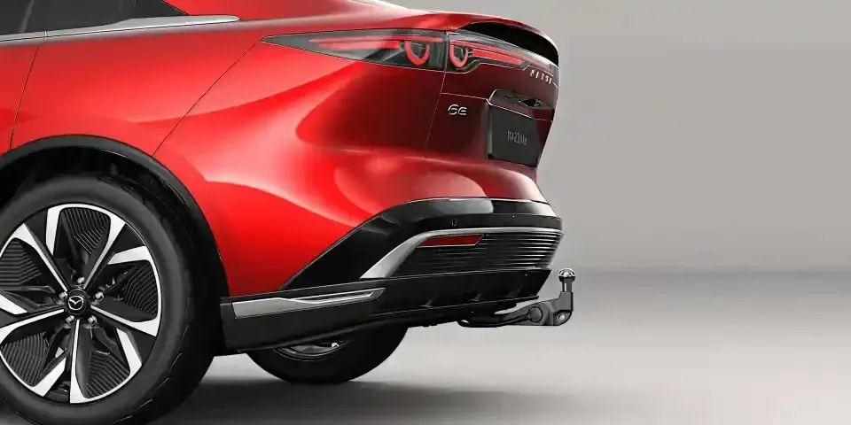 Rear side view of a Soul Red all-electric Mazda 6e hatchback fitted with a towbar for added convenience