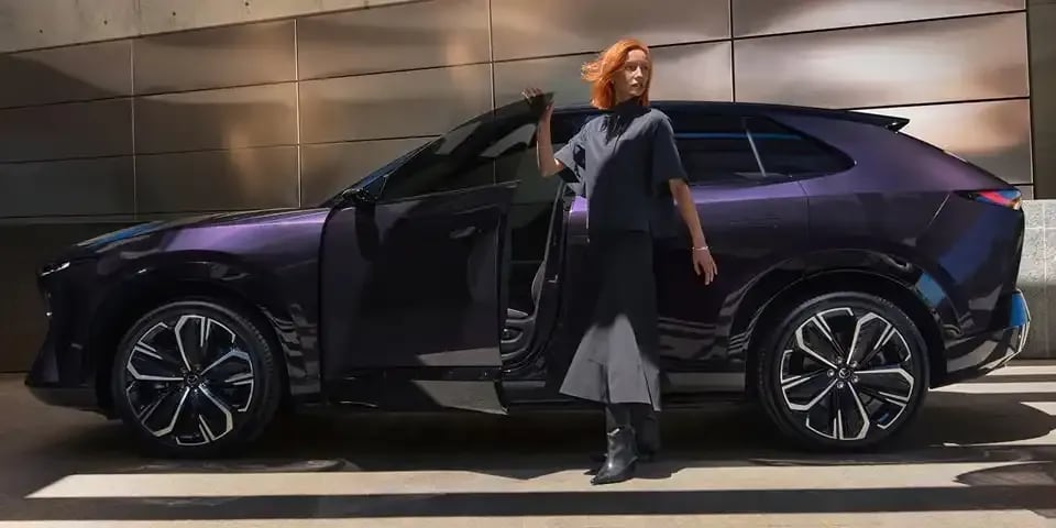 Side view of a Nightfall Violet all-electric Mazda CX-6e SUV with a woman stepping out of the open frameless front door