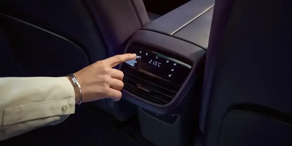 A man's hand controlling the rear climate control air conditioning from the rear centre console of the all-electric Mazda CX-6e SUV