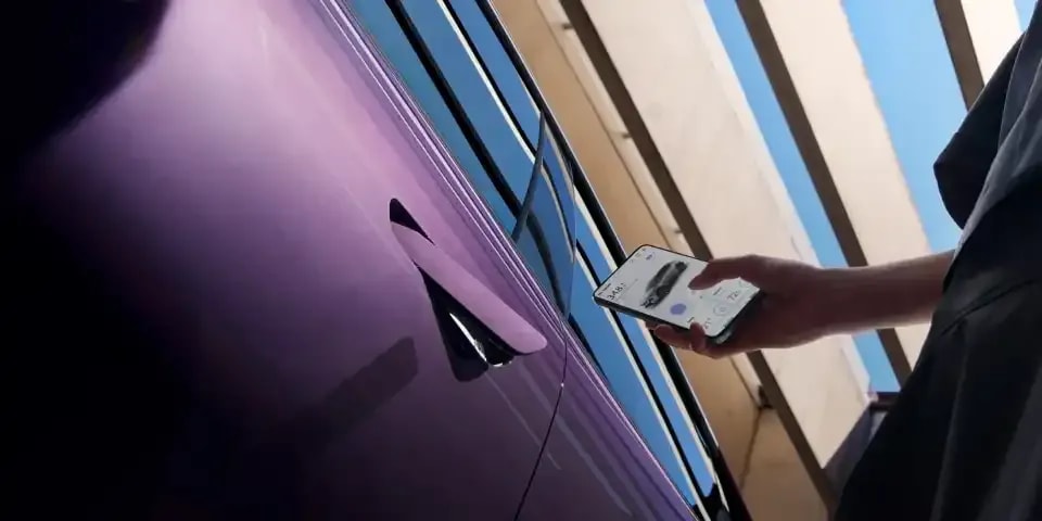 Close up of a smartphone being held next to the front door of a Nightfall Violet all-electric Mazda CX-6e to unlock the car with the phone key 