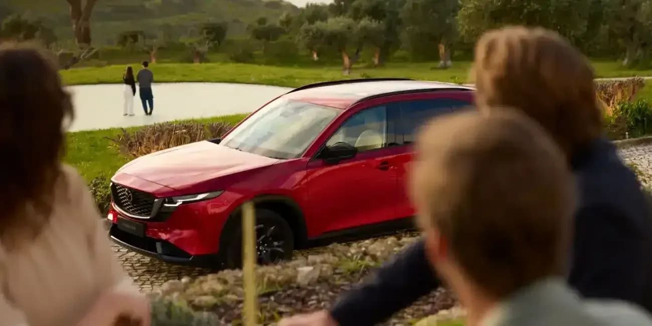 Front three quarter view of a Soul Red Mazda CX-5 SUV parked on a cobblestone driveway with people in the foreground and background