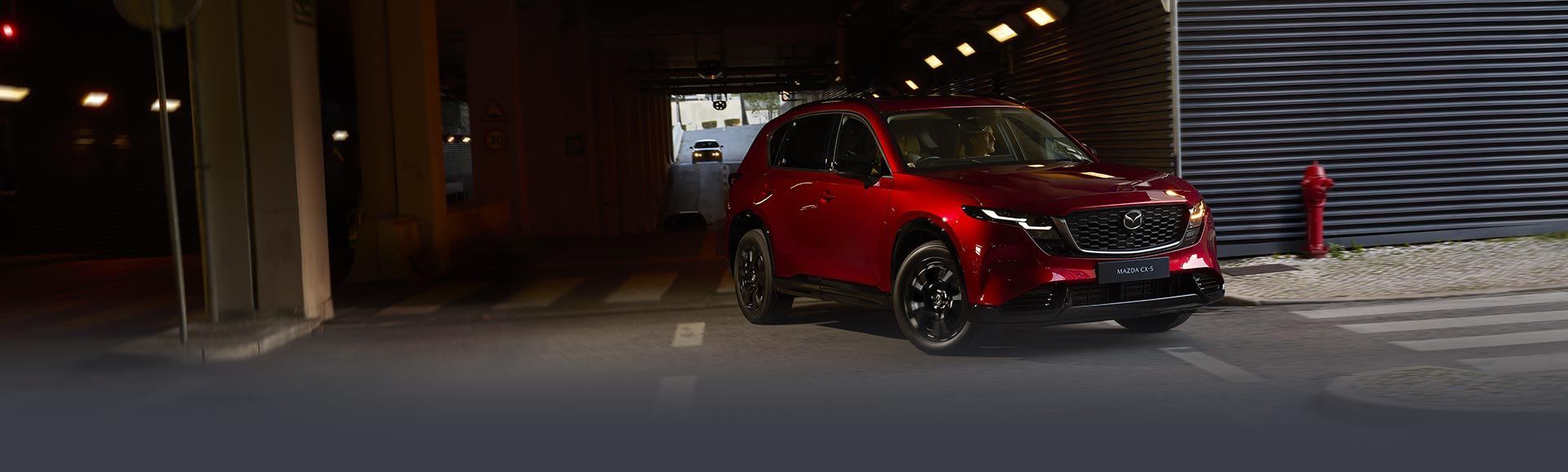 Front three quarter view of a Soul Red Mazda CX-5 turning left when exiting a tunnel