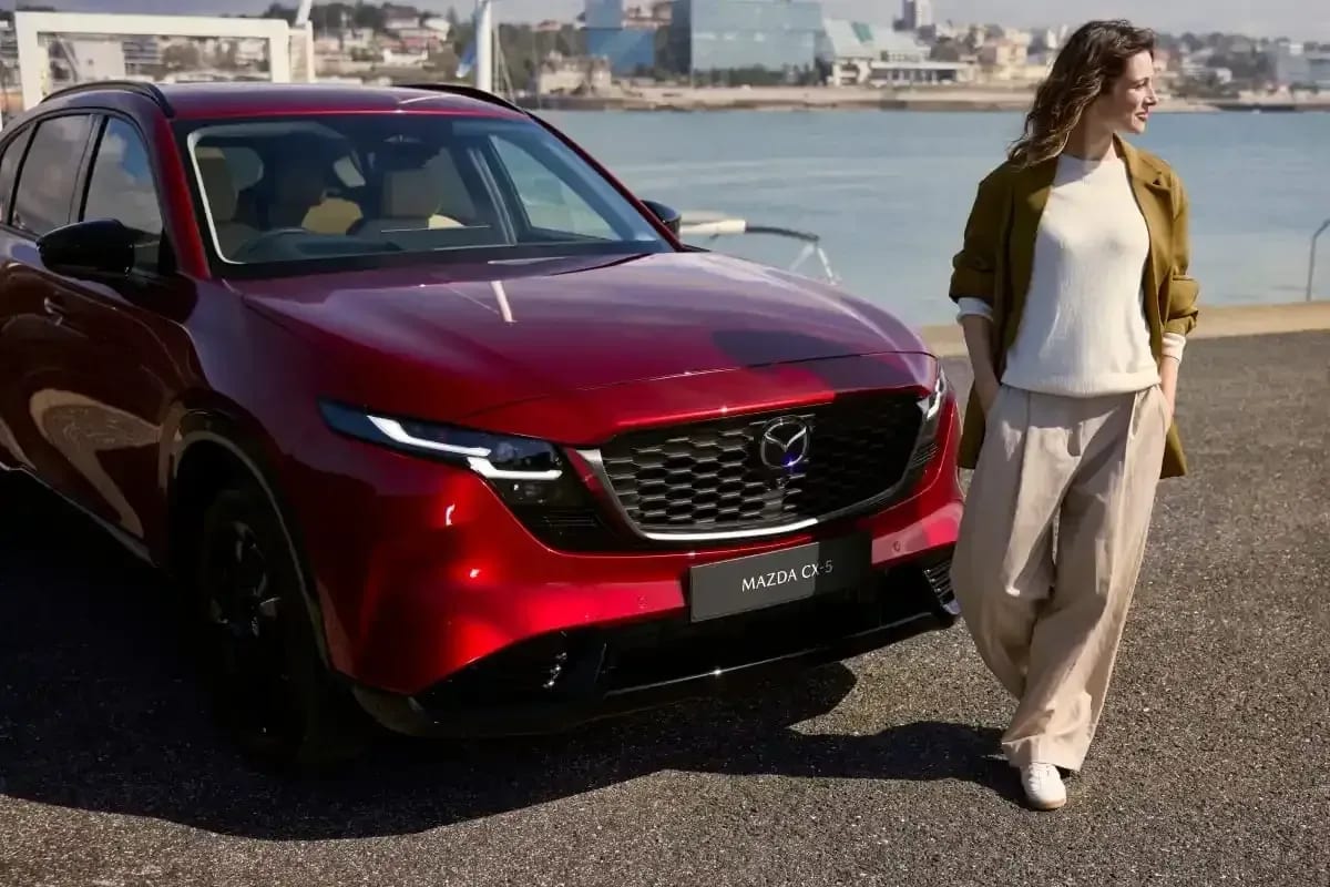 Front grille of a stationary Soul Red Mazda CX-5 with a woman walking in front of the car