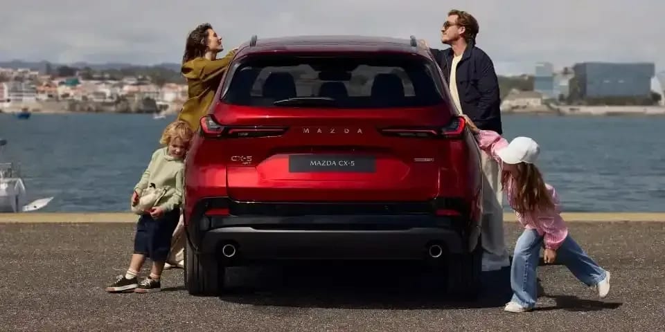 Rear view of a Soul Red Mazda CX-5 parked next to a harbour with a man and woman and their two children standing around the car